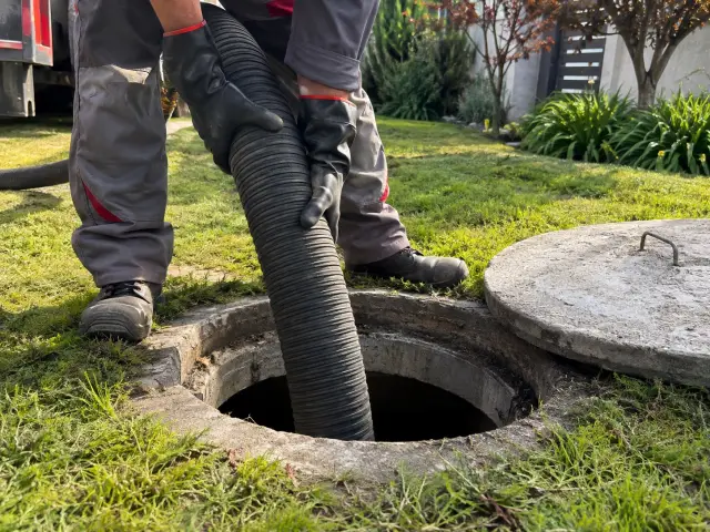 Manos con guantes metiendo una manguera de succión en una fosa abierta